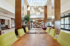 A spacious lobby with a long wooden conference table, green upholstered chairs, and a modern chandelier.