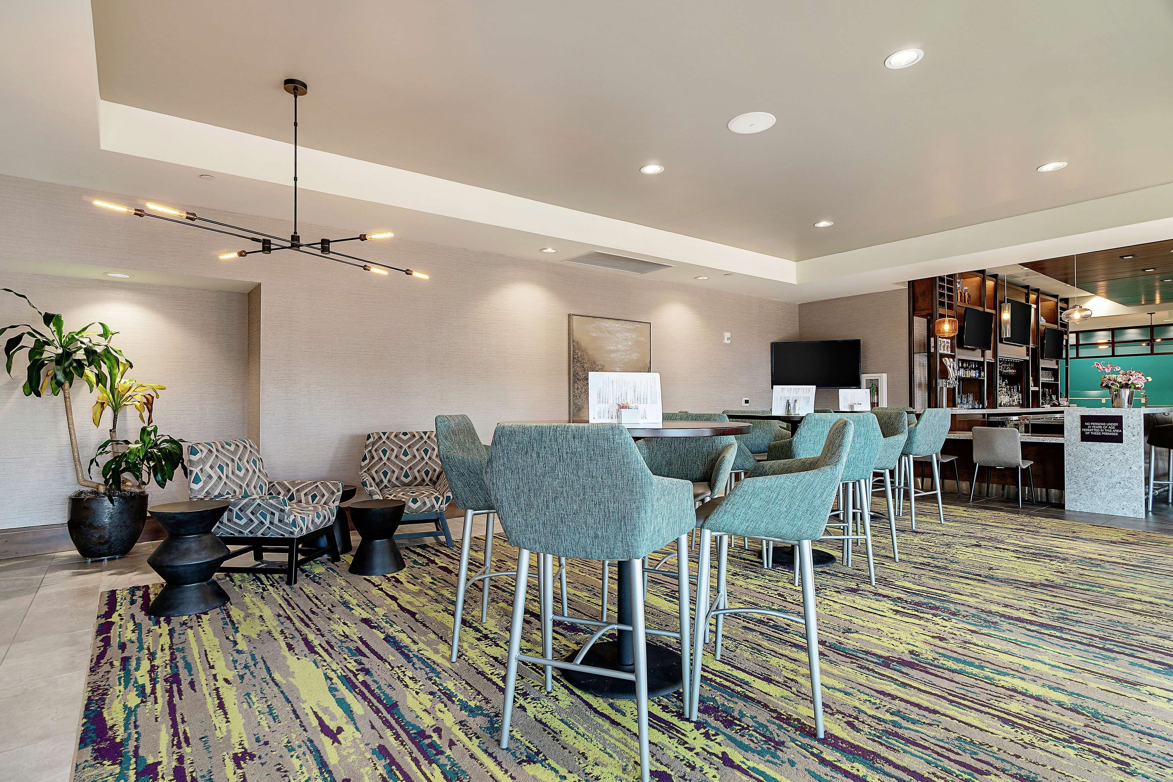 Un hall d’hôtel moderne doté d’un bar, de coins salon et d’un comptoir d’accueil.