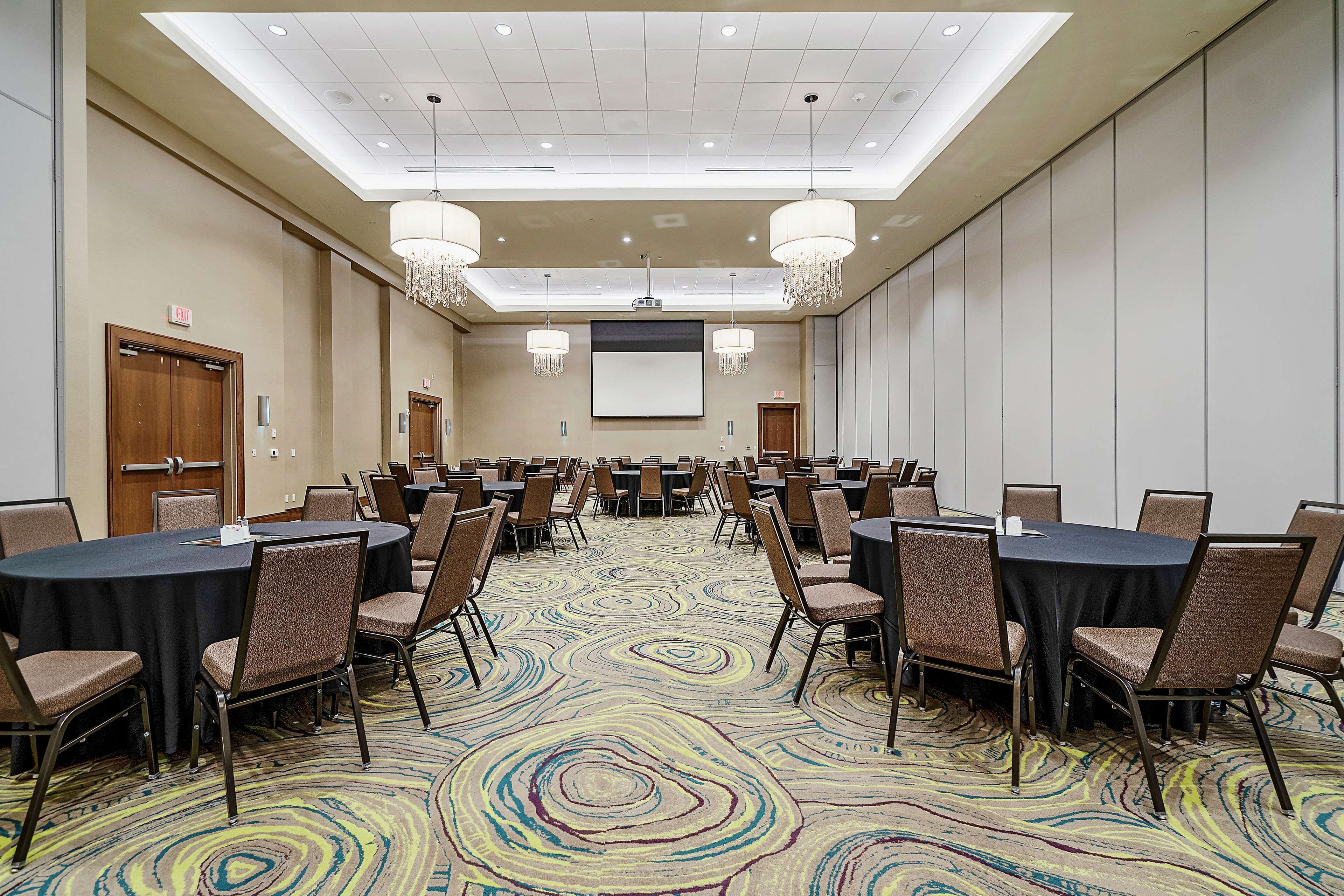 Un salón de conferencias con mesas y sillas redondas, una pantalla de proyector y candelabros.