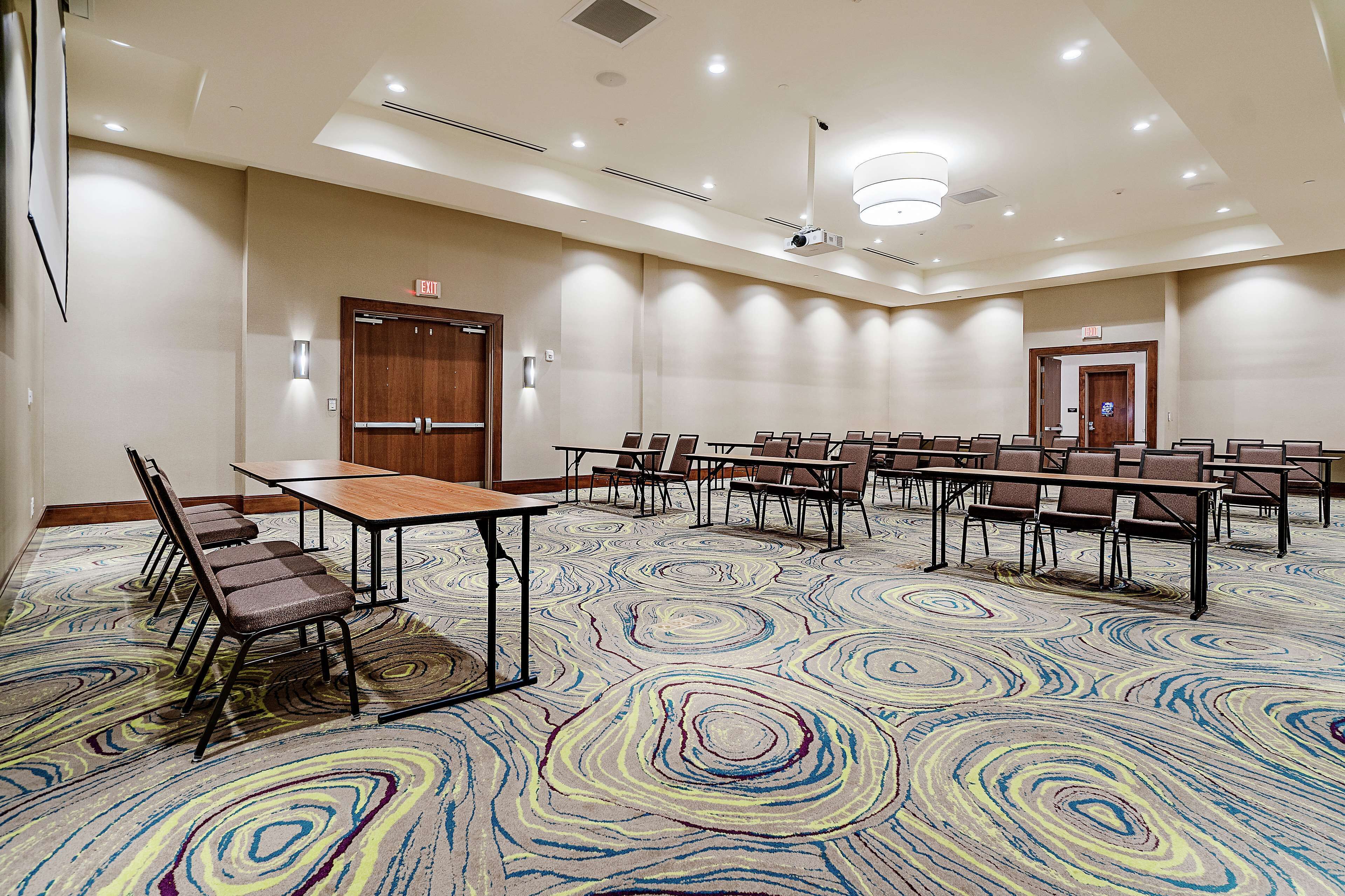 Une salle de conférence dotée d’un tapis à motifs, de tables, de chaises et d’un projecteur fixé au plafond.