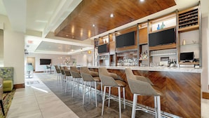 A modern bar area with a wooden ceiling, bar stools, and a variety of bottles and glasses. - Hilton Garden Inn Edmond / Oklahoma City North, OK (Edmond)