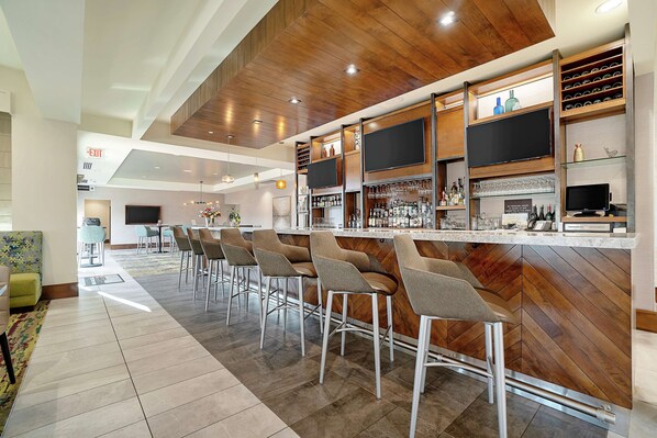 A modern bar area with a wooden ceiling, bar stools, and a variety of bottles and glasses.