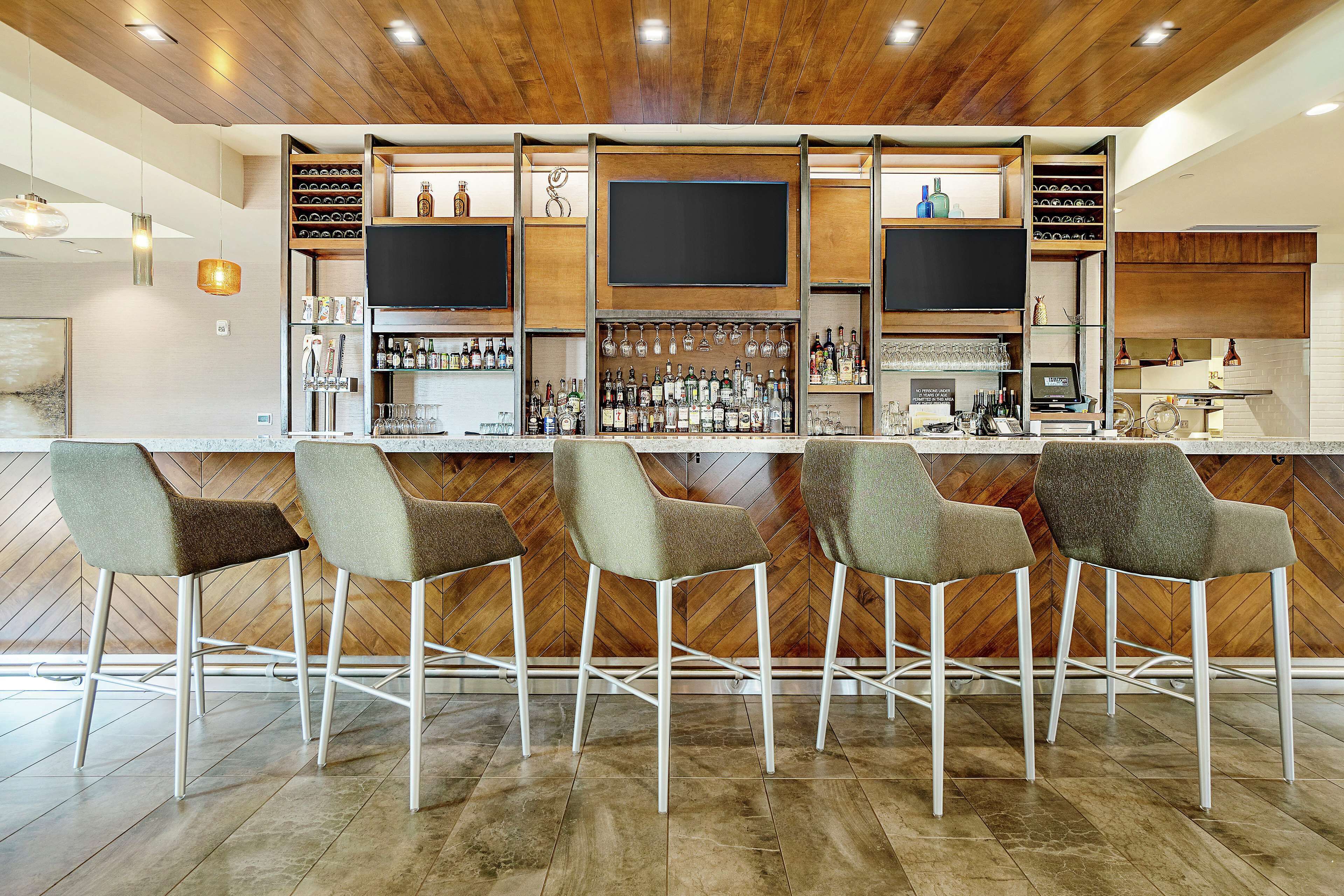 A bar area with a wooden ceiling, multiple shelves with bottles, and bar stools.