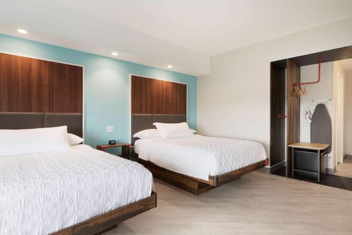 A hotel room with two beds, a wooden headboard, a small table, and a shower area.