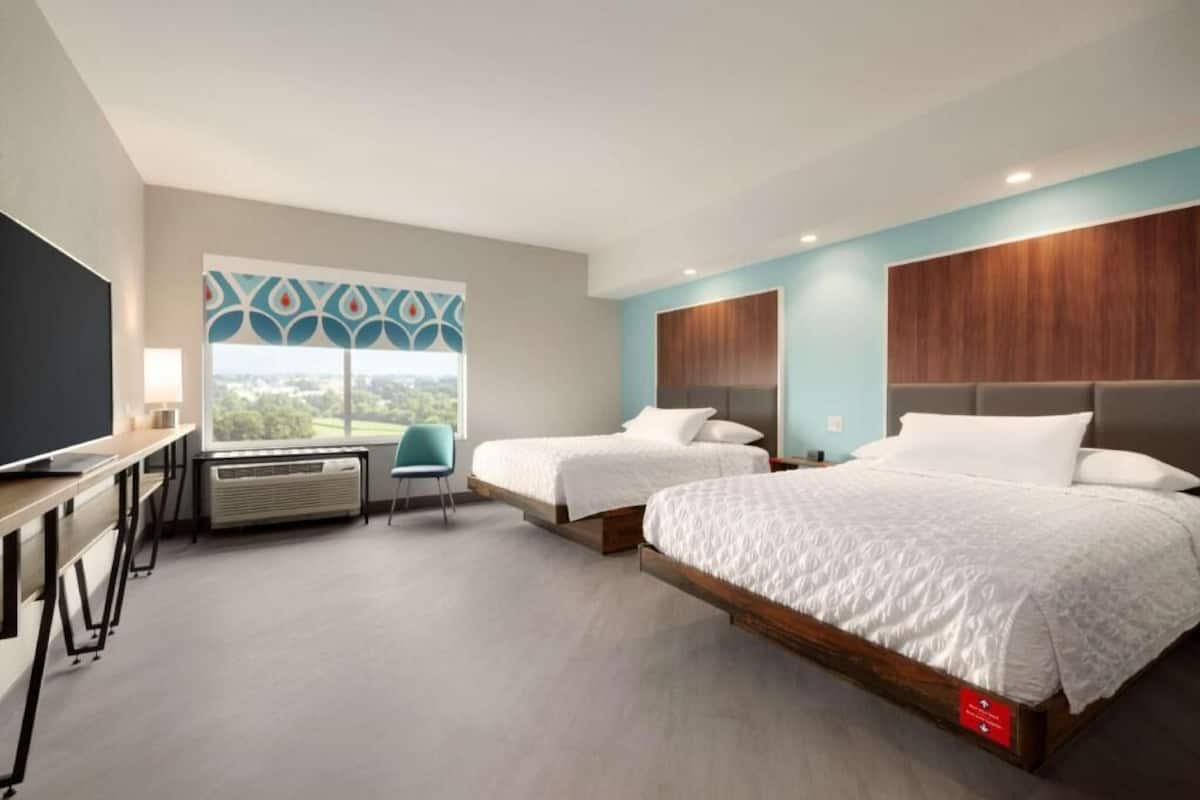 A hotel room with two beds, a desk, a chair, a TV, and a window with a view.