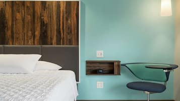 A bedroom with a bed, a wooden headboard, a teal wall, a small shelf, and a chair.