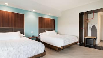 Habitación de hotel con dos camas, cabeceros de madera, una mesita y zona de ducha.