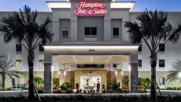 Un bâtiment de la chaîne Hampton Inn & Suites, doté d'une façade moderne, d'une enseigne au néon bien visible et d'une entrée bien éclairée.