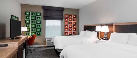 A hotel room with two beds, a desk, a chair, and a TV.