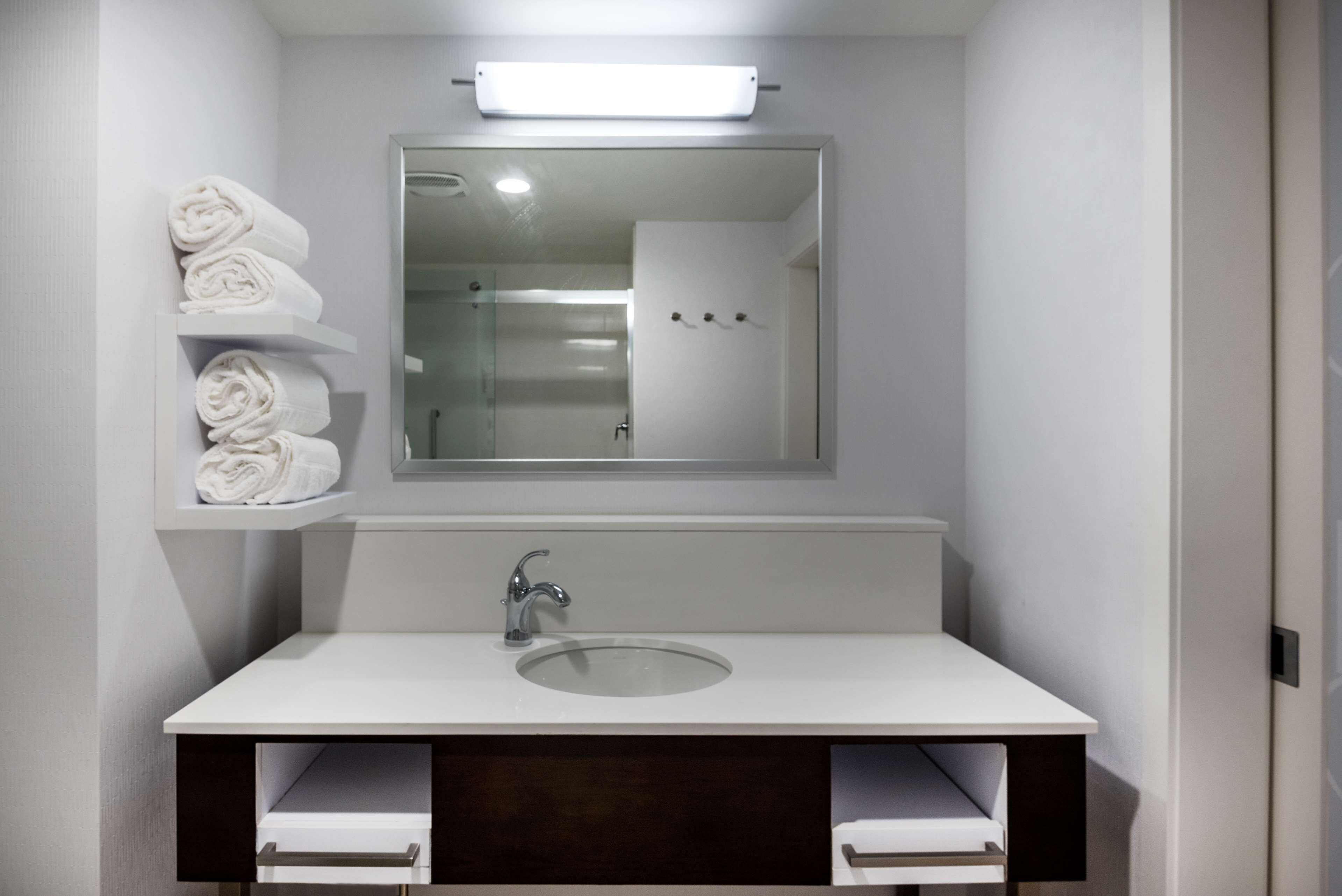 A modern bathroom with a white sink, a mirror above it, and a towel rack with folded towels.