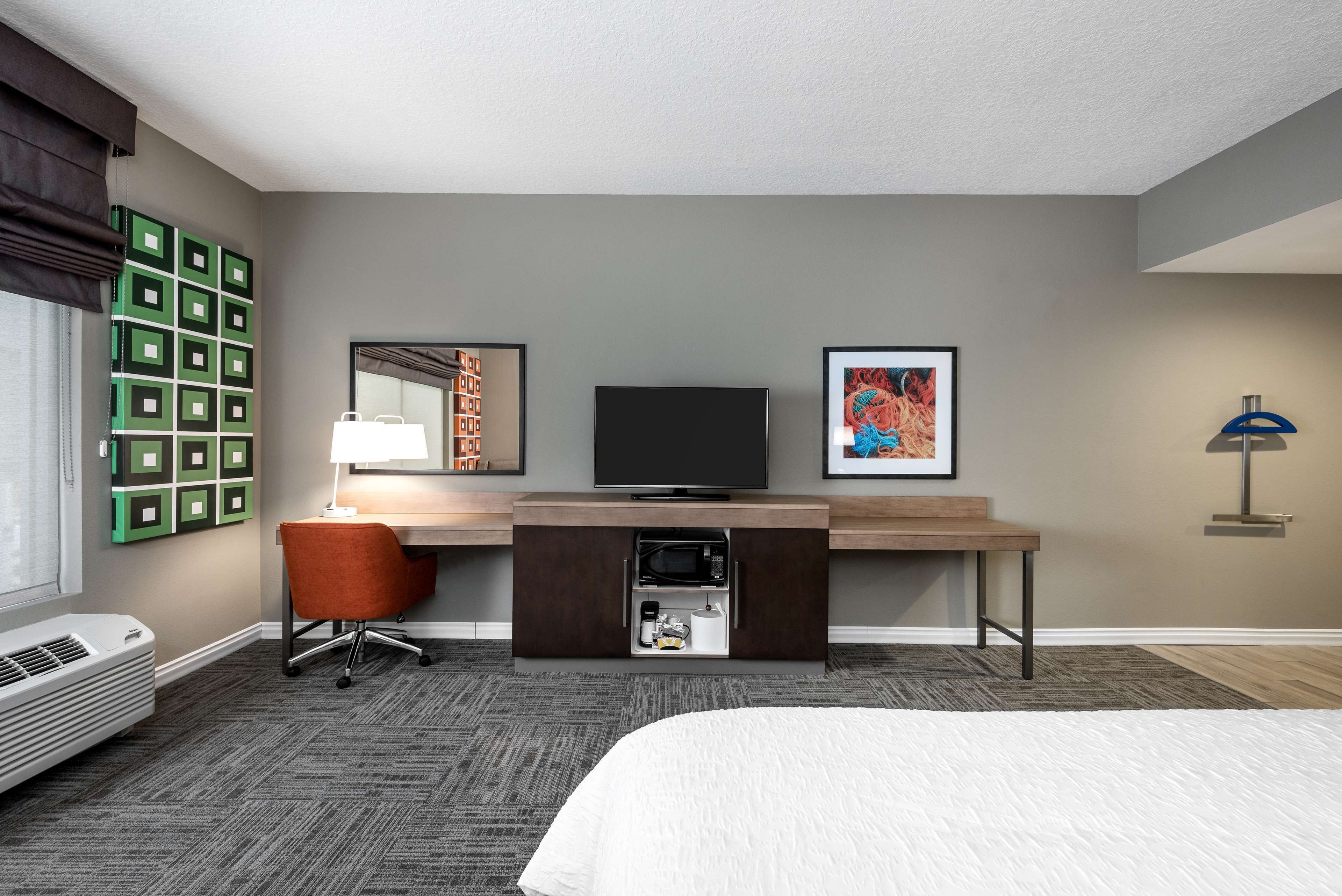 A hotel room with a bed, a desk with a computer, a chair, a TV, a microwave, and a coffee maker.