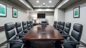 Une salle de conférence dotée d’une grande table rectangulaire entourée de fauteuils en cuir noir, d’un téléviseur à écran plat fixé au mur et d’œuvres d’art encadrées qui décorent les murs.