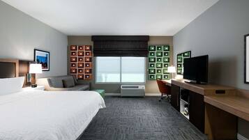 Una habitación de hotel con cama, escritorio, televisor, ventana y espacios de almacenamiento.