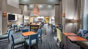 Un hall d’hôtel doté de plusieurs espaces aménagés avec des sièges, notamment des tables et des chaises, une grande table à manger centrale et un grand miroir.