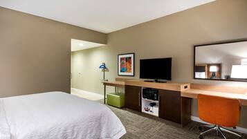 Habitación de hotel con cama, escritorio con televisor, reposapiés verde y espejo.