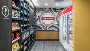 Un rayon consacré aux en-cas, avec des étagères remplies de divers types de chips et de produits à grignoter, un mur orné d’une enseigne « Friandises », et un présentoir réfrigéré.