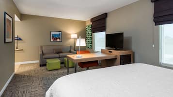 Habitación de hotel con una cama grande, un escritorio con lámpara, un televisor, un sofá y un taburete verde.