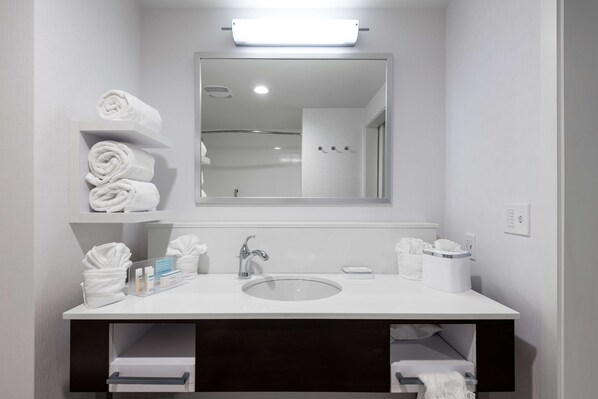 A modern bathroom with a white sink, a mirror, and shelves holding towels. - Hampton Inn & Suites West Melbourne-Palm Bay Road (Melbourne)