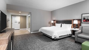 Une chambre d’hôtel avec un lit, un bureau, une télévision, une chaise et une lampe.