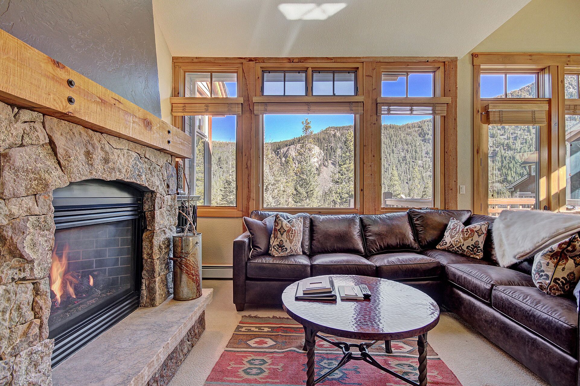 A cozy living room with a stone fireplace, leather sofa, and large windows offering mountain views.