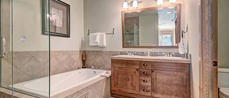 A bathroom with a glass-enclosed shower, a wooden vanity with a large mirror, and a white bathtub.