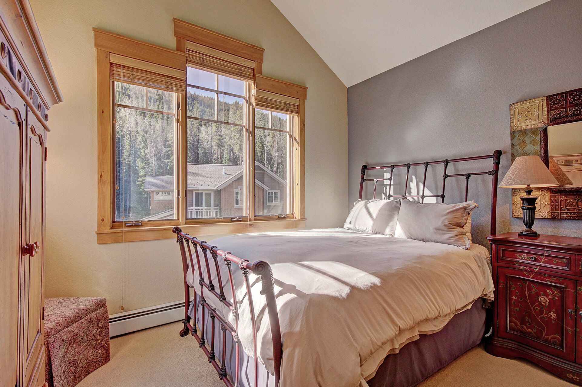 A bedroom with a large window, a bed, a nightstand, and a dresser.