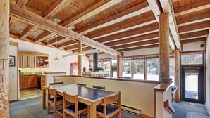 A spacious kitchen with wooden cabinets, a dining area with a large table and chairs, and a view of a snowy landscape through large windows. - 2035 Stead 2 Bedroom Condo by RedAwning (Keystone)