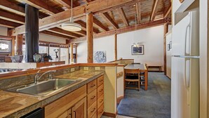 A kitchen with wooden cabinets, a sink, and a stove. There is a dining area with a table and chairs. - 2035 Stead 2 Bedroom Condo by RedAwning (Keystone)