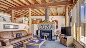 A cozy living room with a stone fireplace, leather sofa, and a television. - 2035 Stead 2 Bedroom Condo by RedAwning (Keystone)