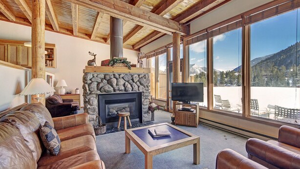 A cozy living room with a stone fireplace, leather sofas, a coffee table, and a large window offering a mountain view. - 2035 Stead 2 Bedroom Condo by RedAwning (Keystone)