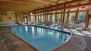 An indoor swimming pool with clear blue water, surrounded by lounge chairs and large windows offering views of the outdoors. - 2035 Stead 2 Bedroom Condo by RedAwning (Keystone)