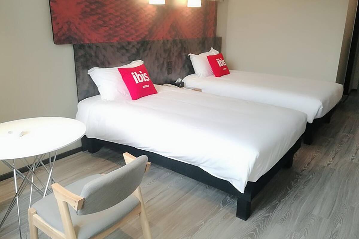 Et hotelværelse med to senge, et lille rundt bord og en stol.