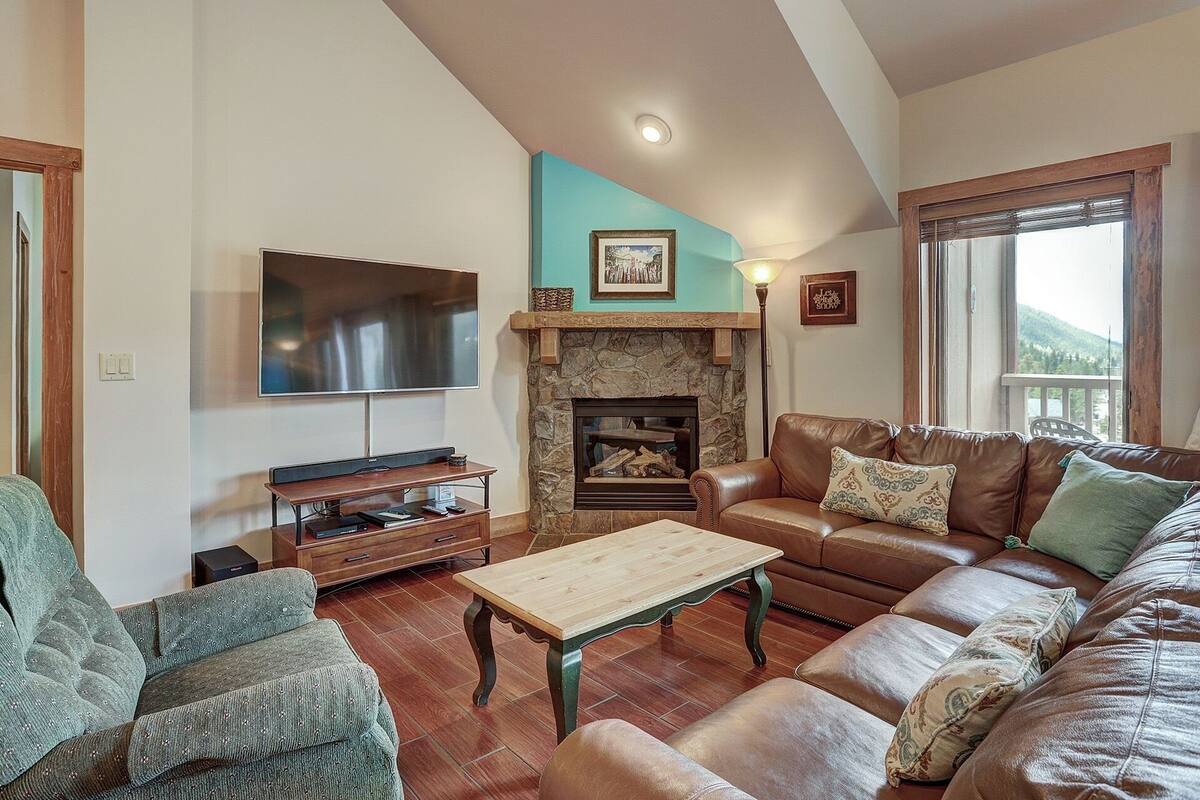 Una sala de estar con chimenea de piedra, sofá de cuero y televisor montado en la pared.