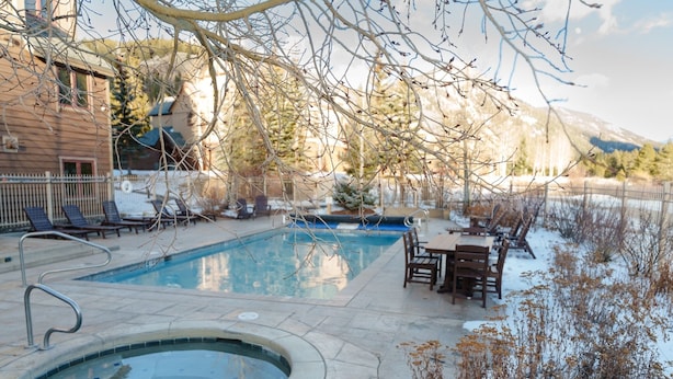 A swimming pool with a hot tub, surrounded by lounge chairs and a table, with a mountain backdrop. - 2296 Red Hawk Lodge 2 Bedroom Condo by RedAwning (Keystone)