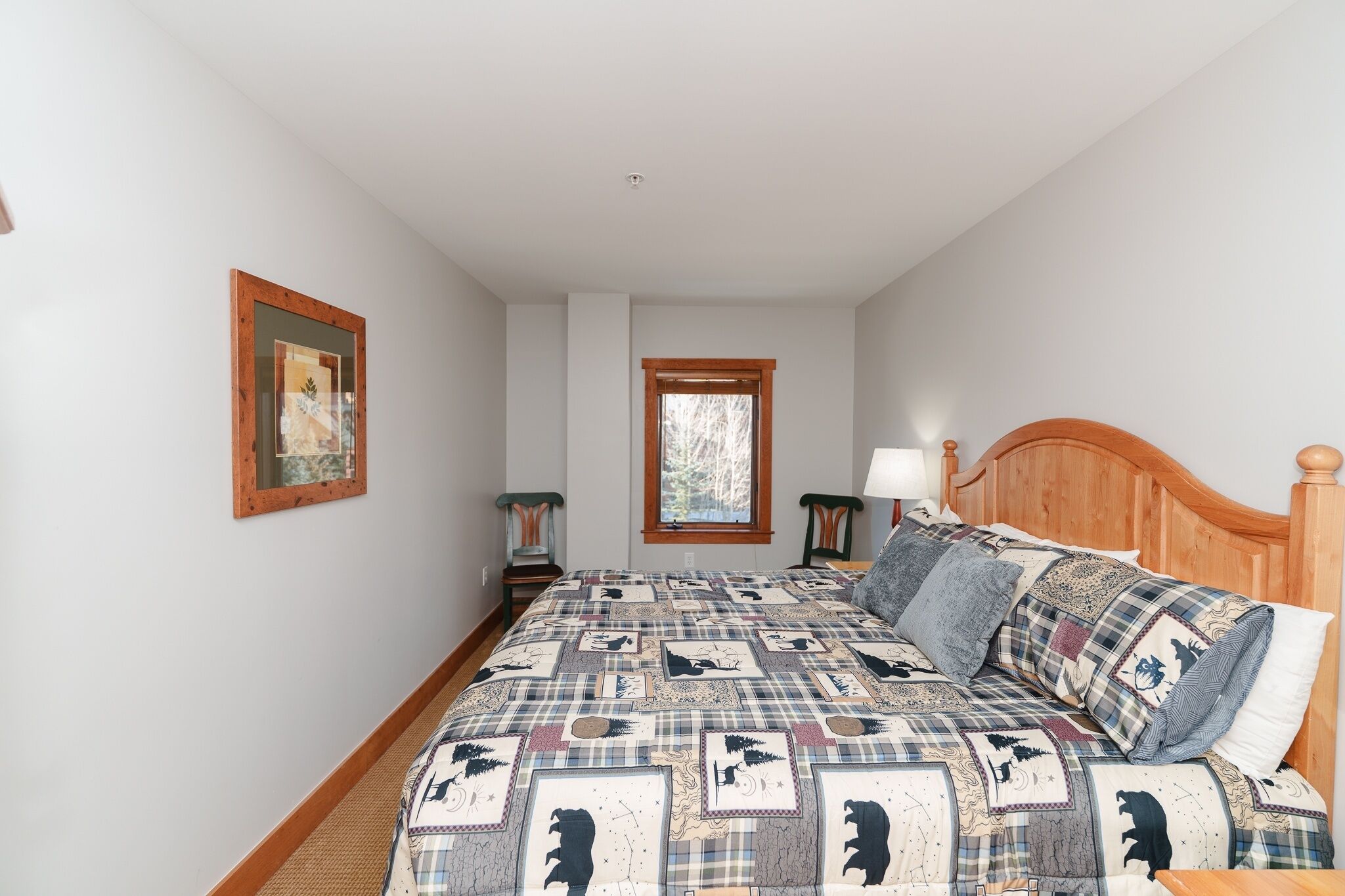 A bedroom with a large bed, a window, a framed picture, and two bedside tables.