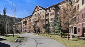 A multi-story hotel with a stone facade, balconies, and a central courtyard with trees and a fire hydrant. - 2296 Red Hawk Lodge 2 Bedroom Condo by RedAwning (Keystone)