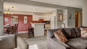 Een moderne woonkamer met een grijze bank en een eethoek met een houten tafel en stoelen.