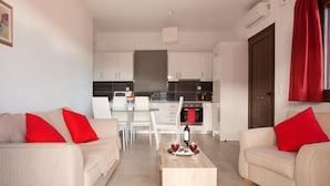A modern living room with two beige sofas, each with a red pillow, and a wooden coffee table in the center. - Daphne-Morfi Village (Apokoronas)