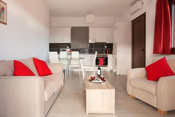 A modern living room with two beige sofas, each with a red pillow, and a wooden coffee table in the center.