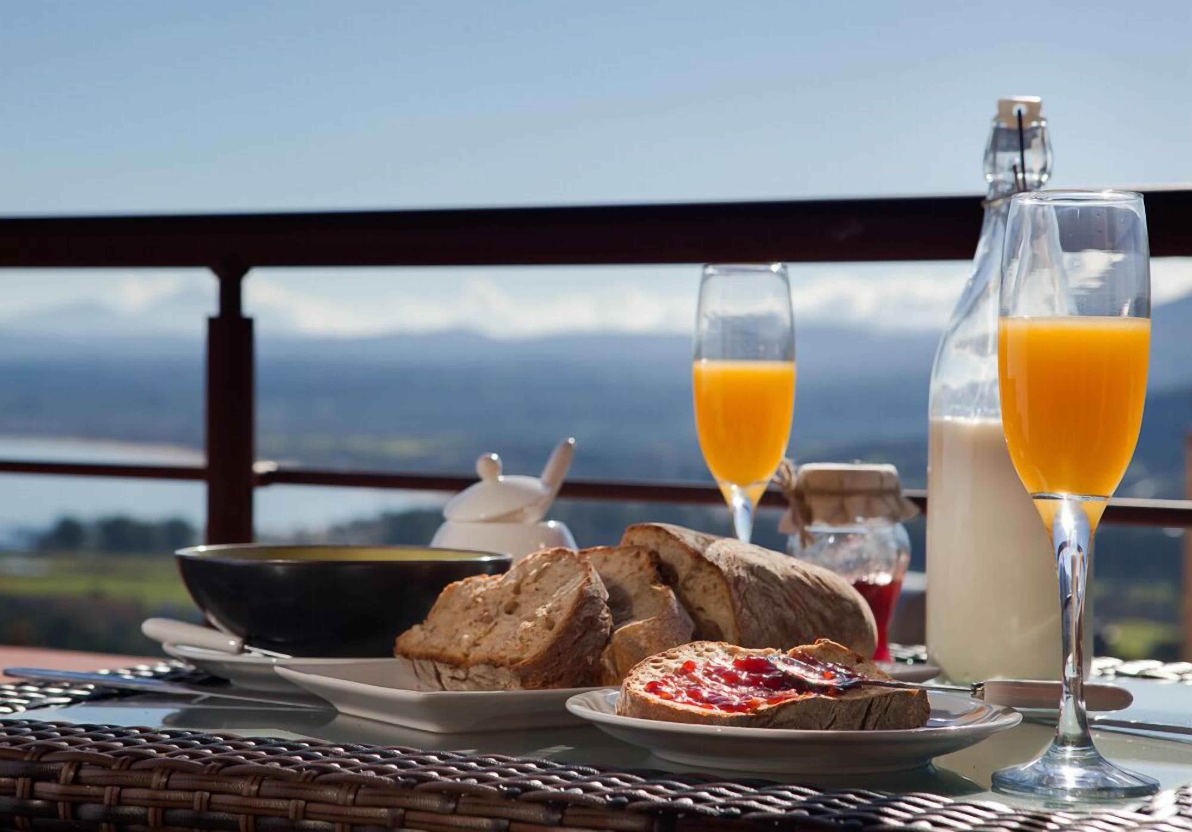 A breakfast setting with bread, butter, jam, and orange juice on a table with a scenic view.