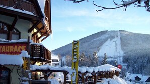 A snow-covered mountain with a ski lift and a building with a sign reading "TAURACE". - Pension Rotunda (Harrachov)