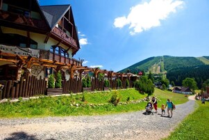 A traditional wooden building with a balcony, a gravel path, and a mountainous backdrop.