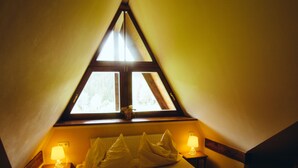 A cozy bedroom with a sloped ceiling, a bed with pillows and a folded towel, two bedside lamps, and a window with a view. - Pension Rotunda (Harrachov)