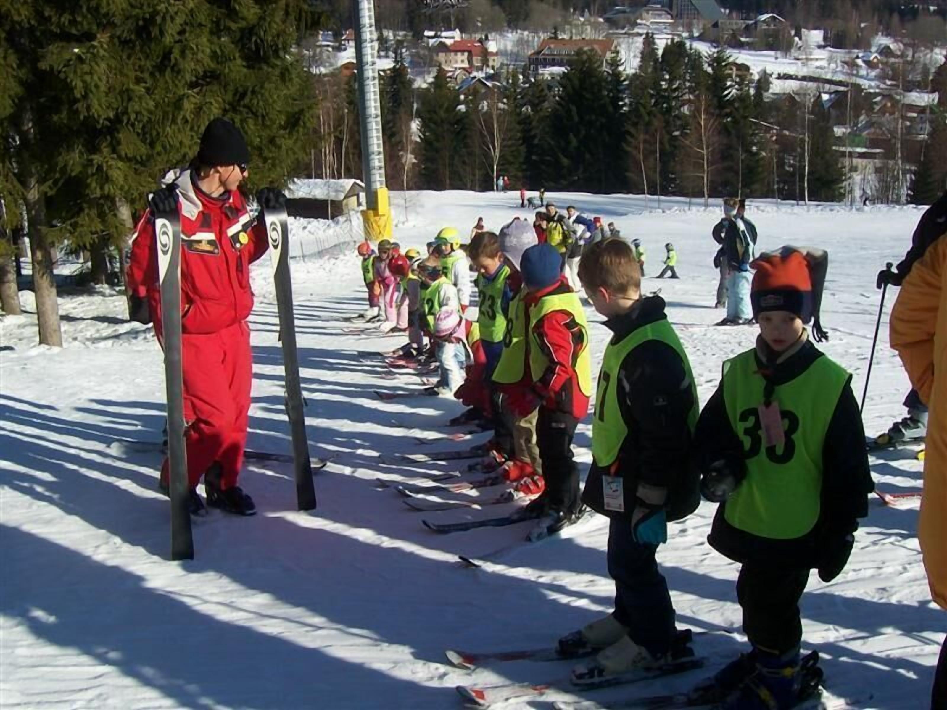 Un groupe d’enfants, équipés de skis, se tient en rang sur une pente enneigée, probablement en préparation pour un cours de ski ou un événement.