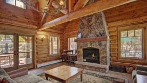 A log cabin interior with a stone fireplace, wooden furniture, and large windows. - 6532 Settlers Creek Townhomes 2 Bedroom Condo by RedAwning (Keystone)