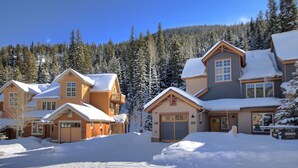 A snow-covered residential area with multiple houses, each featuring a distinct architectural style, surrounded by a forested mountain backdrop. - 6532 Settlers Creek Townhomes 2 Bedroom Condo by RedAwning (Keystone)