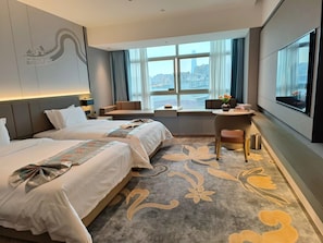 A hotel room with two beds, a seating area, a desk, and a large window with a city view. - Global Business Hotel (Dongguan)