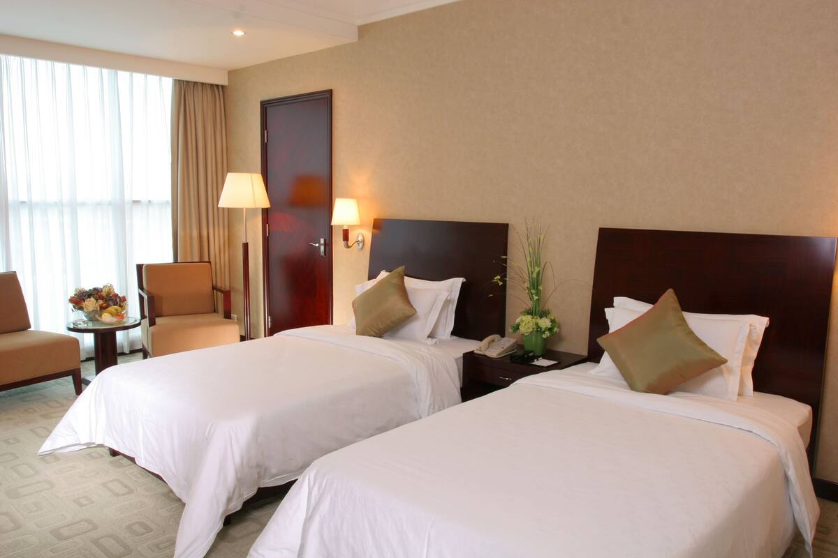 A hotel room with two beds, a desk, a chair, a lamp, and a window with curtains.