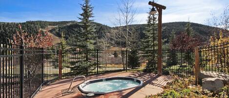 A hot tub on a patio with a metal fence and a view of a forested mountain range.