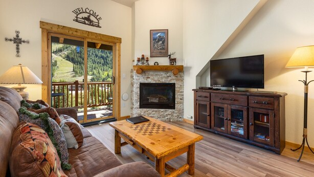 A cozy living room with a fireplace, a TV, and a chessboard on a wooden table. - 2674 Tenderfoot Lodge 2 Bedroom Condo by RedAwning (Keystone)